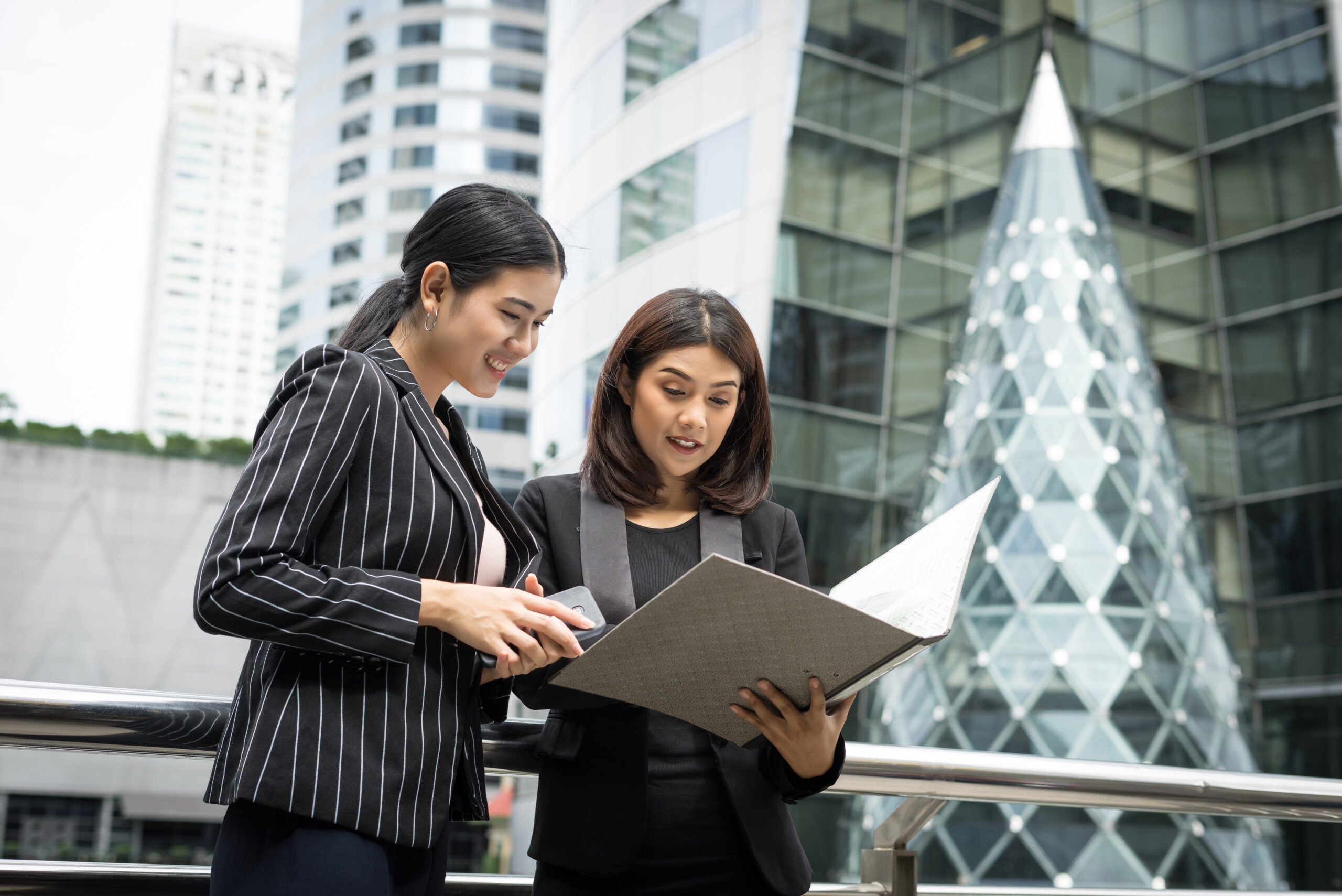Businesswomen discussing over paperwork together against railing